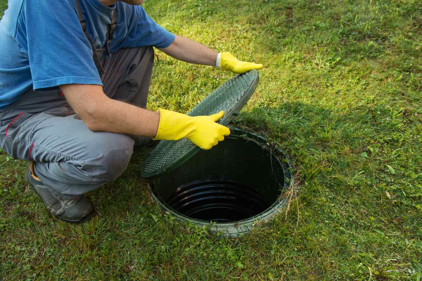 vidage-fosse Personne inspectant une trappe de fosse septique sur pelouse.